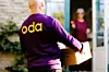 Oda-bud i lilla genser bærer eske mot kunde i åpen ytterdør