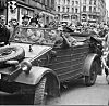 Tre militære i bil følges av unge gutter, tett med tilskuere langs Karl Johan, Oslo, mai 1945,