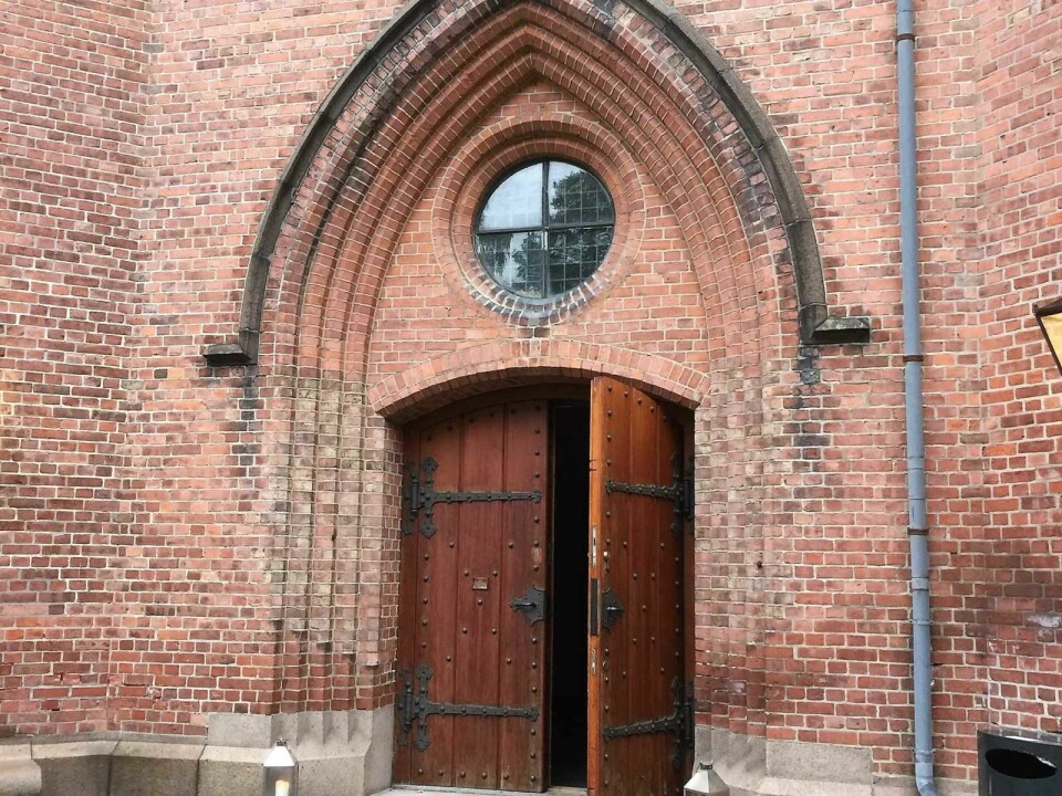 Rød teglstein og tunge tredører viser vei inn i kirken som skal ha 12.500 registrerte sognebarn. Foto: Kjersti Opstad