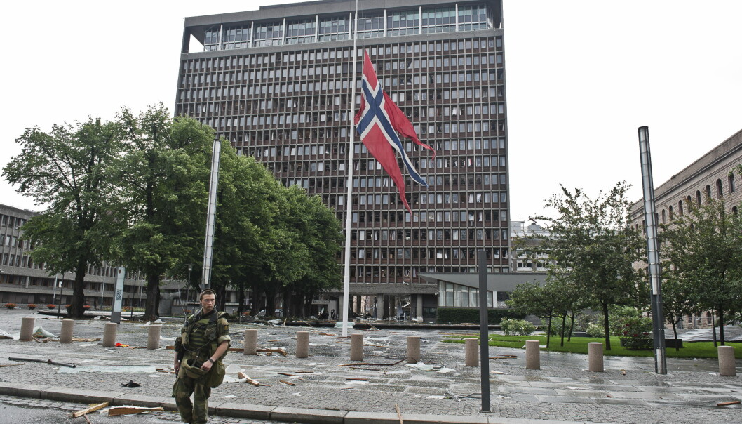 Flagget på halv stang foran et ødelagt regjeringskvartal 22. juli 2011. I dag blir navnene på alle de 77 drepte lest opp.