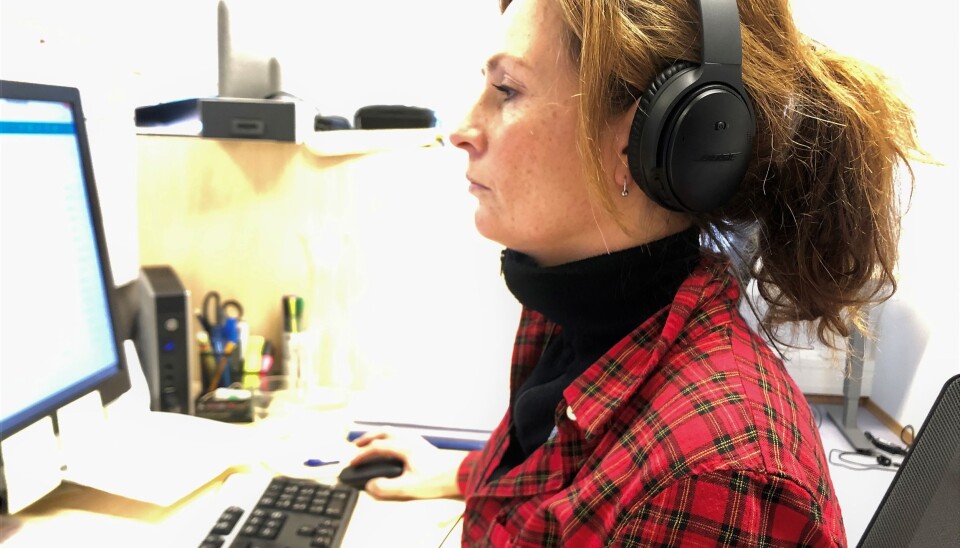 Sykepleier Dagrun Norbakken sitter i telefon med øreklokker på i kontorlandskapet når hun snakker med smittede og nærkontakter og samtidig logger alt i datasystemet.