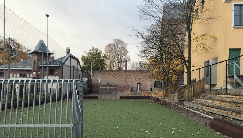 Skolens hovedbygninger ligger bak muren bakerst i bildet. Den lille ballbanen er også en del av skoleanlegget.