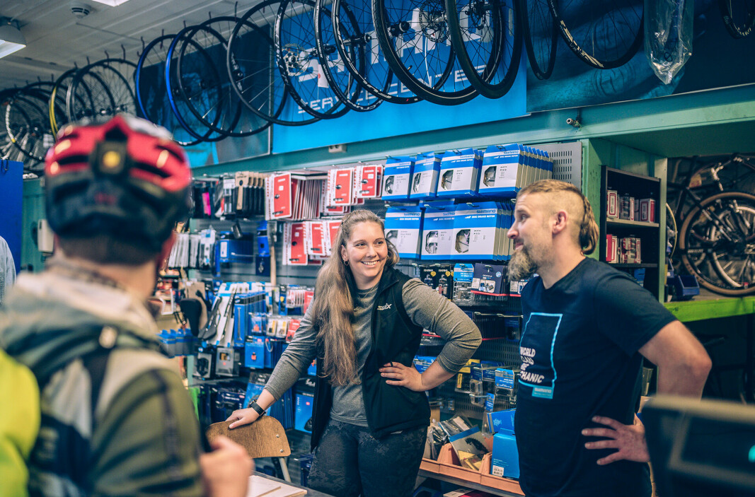 Bak kassa på sykkelverkstedet står de to glade sykkelreparatørene Mia Halvorsrød og Adam Marcin Jurasz.