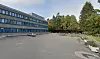 Fasaden på Apaløkka skole med skolegård og skogholt i forgrunnen.