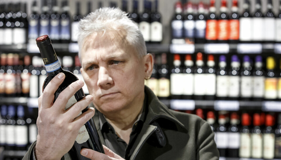 Mann studerer rødvinsflaske på Vinmonopolet. Modellklarert