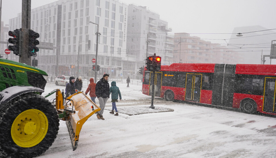 Traktor med snøskjær i snøvær mens buss kjører i kryss i Bjørvika.