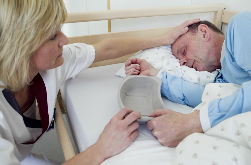 Helsearbeider og mannlig pasient. Pasienten ligger i sengen. Helsepersonell yter omsorg.Illustrasjonsbilde