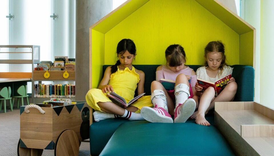 Tre barn leser bøker på biblioteket.