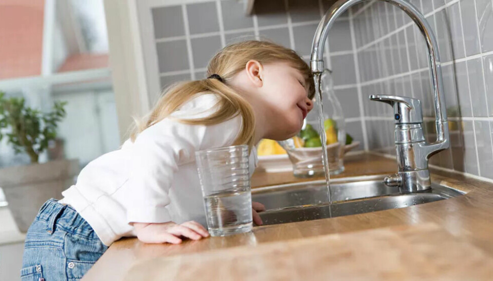 Jente drikker vann fra kjøkkenspringen.