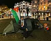 Mann sitter utenfor et telt. Palestina flagg henger over teltet.