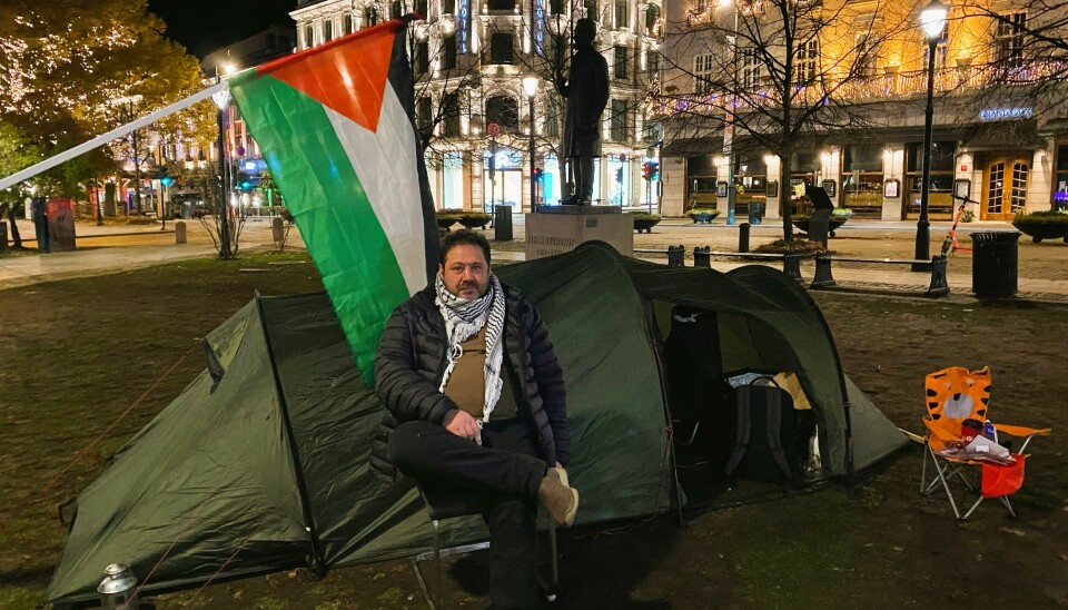 Mann sitter utenfor et telt. Palestina flagg henger over teltet.