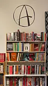 Nærbilde av bokhylle med anarkisme logo over.
